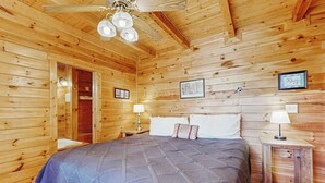 A wooden cabin room with a bed, two bedside tables, a ceiling fan, and framed pictures on the walls. - Wonderland Ellijay Stay (Ellijay)