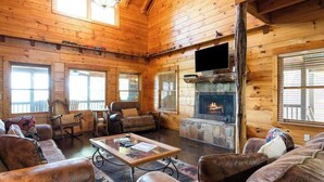 A log cabin interior with a fireplace, leather furniture, and a television mounted on the wall. - Roscoe's Retreat Stay (Blue Ridge)