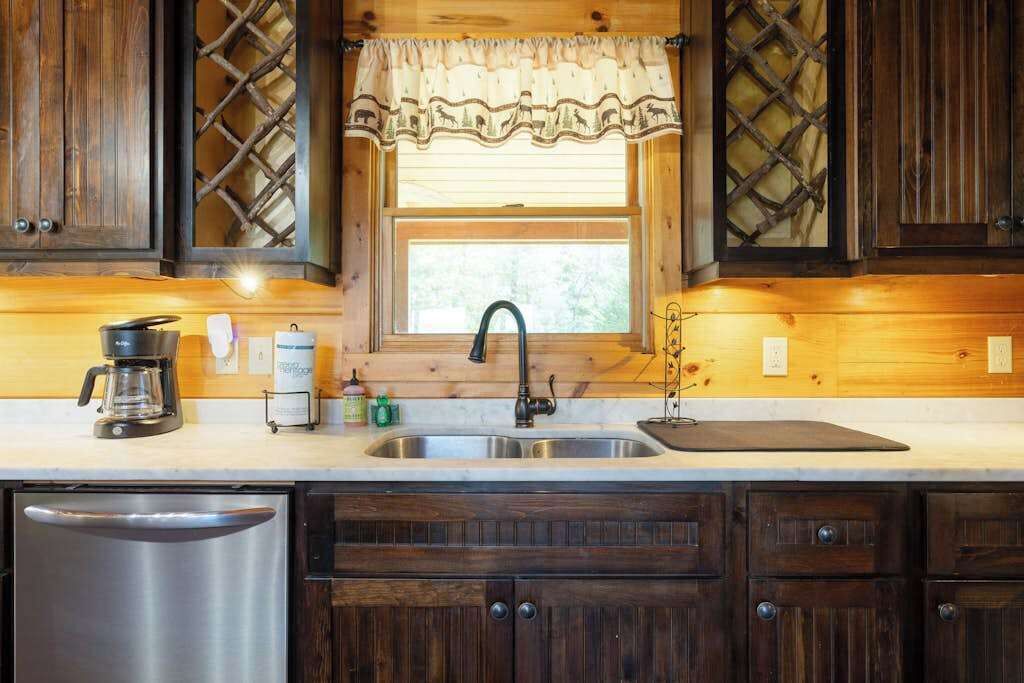 A kitchen with wooden cabinets, a stainless steel sink, a coffee maker, and a window with a decorative valance.