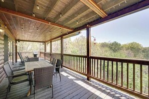 A covered outdoor deck with a table and chairs, wooden beams, and a view of trees. - Cardinal House Retreat (Mineral Bluff)