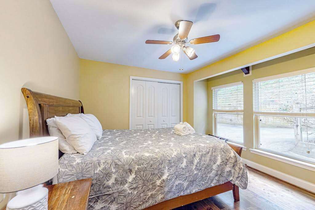 A bedroom with a bed, a ceiling fan, a window with blinds, and a door.