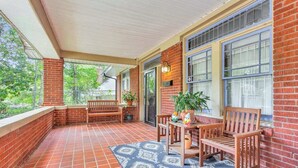 Eine überdachte Terrasse mit Backsteinwänden, großen Fenstern und Gartenmöbeln.