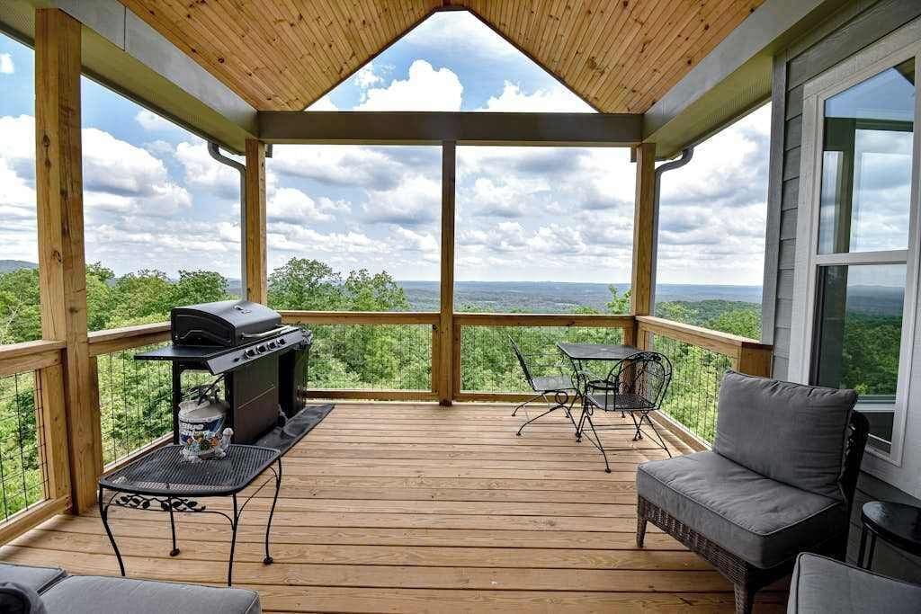 A covered outdoor deck with a grill, seating, and a view of the landscape.
