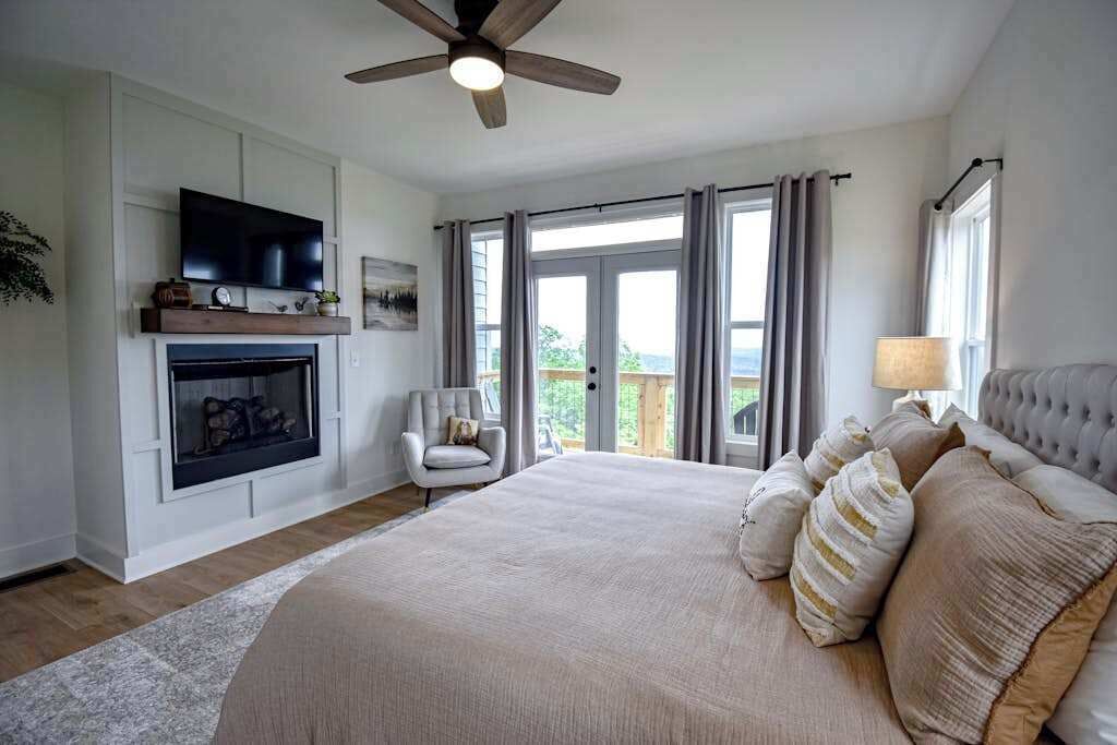Un dormitorio con una cama grande, chimenea, televisión y balcón con cortinas.