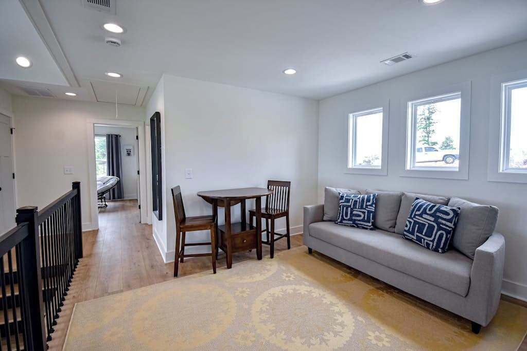 A living room with a sofa, a dining table with chairs, a patterned rug, and a staircase with a railing.