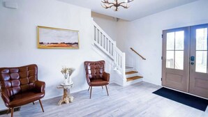 Ein geräumiger Raum mit Holzboden, einer Treppe und zwei Ledersesseln.