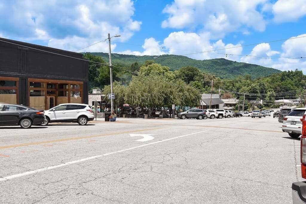 Une intersection avec un bâtiment sur la gauche, un parking rempli de voitures et, en arrière-plan, un paysage montagneux.