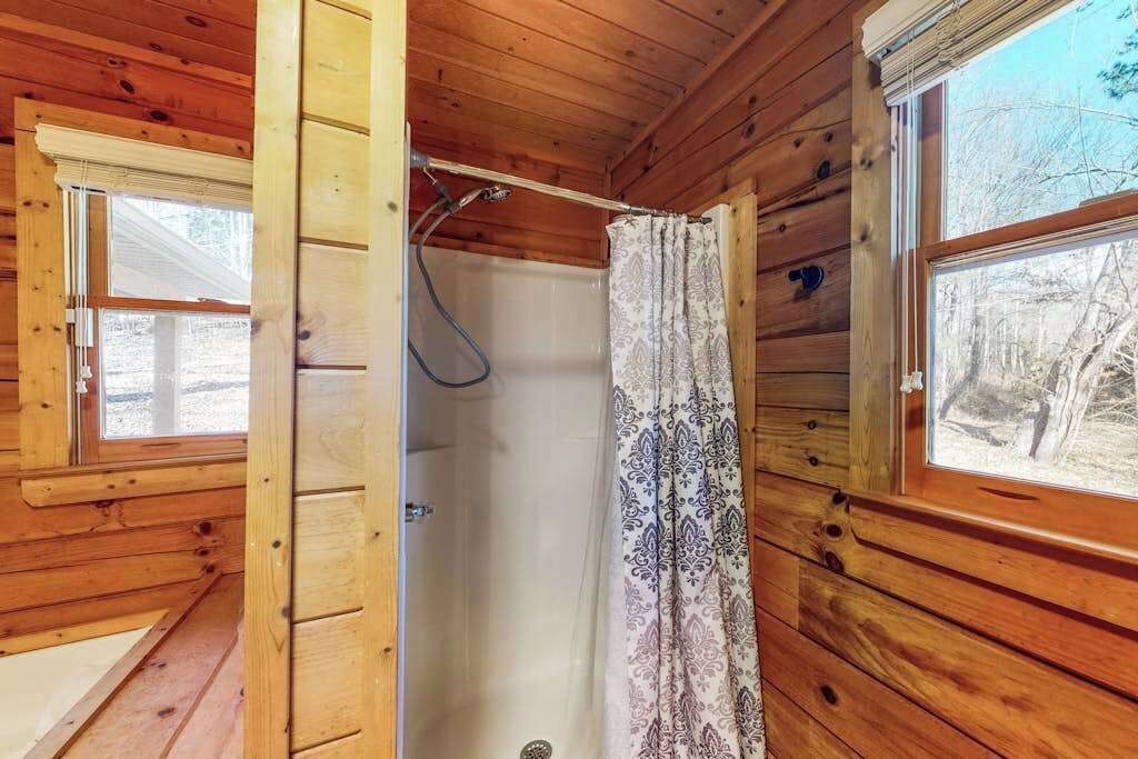 L’intérieur d’une cabane en bois, avec une douche, une fenêtre et une porte.