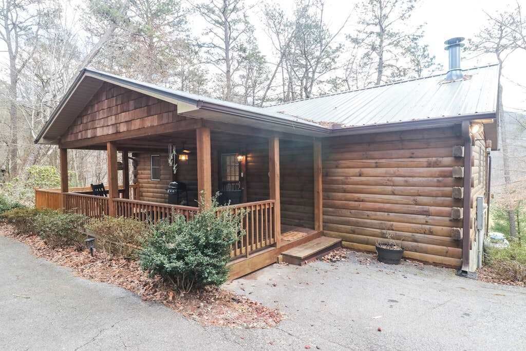 Une cabane en rondins avec une véranda, une cheminée et un petit jardin.