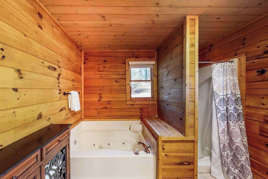 Une salle de bain rustique, avec des murs en bois, comprenant une baignoire, une fenêtre et un rideau de douche.