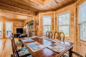 L’intérieur d’un chalet en bois comprend une table à manger, des chaises, une cheminée et de grandes fenêtres.