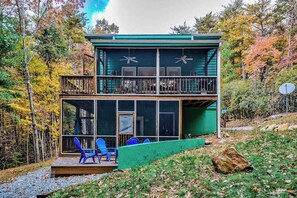 Une cabane à deux étages dotée d’un balcon, de grandes fenêtres et d’une terrasse avec des chaises.