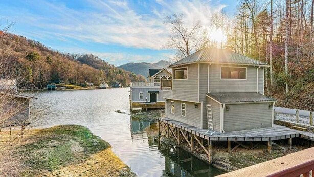 A houseboat with a deck, a small cabin, and a dock extending into a calm lake surrounded by trees and hills. - Timpson Cove Haven Stay (Clayton)