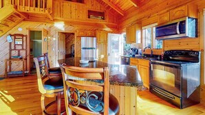 A wooden cabin interior with a kitchen, dining area, and a staircase. - Timpson Cove Haven Stay (Clayton)