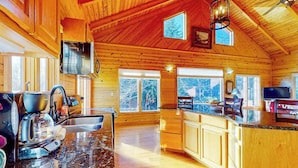 A log cabin interior with a kitchen, dining area, and large windows. - Timpson Cove Haven Stay (Clayton)