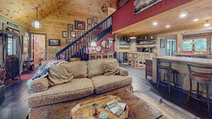 A cozy cabin interior with a wooden ceiling, a staircase, a living area with a sofa and coffee table, and a kitchen area with bar stools. - It's a Wonderful Life (Sautee Nacoochee)