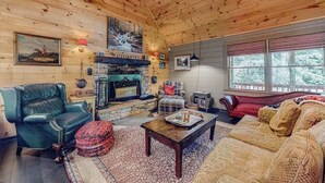A cozy cabin interior with a stone fireplace, leather furniture, and a large window. - It's a Wonderful Life (Sautee Nacoochee)