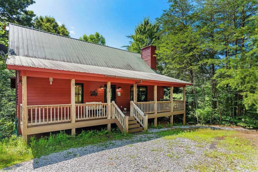 A wooden cabin with a metal roof, a porch, and a chimney.