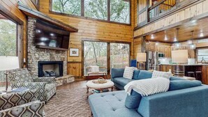 A spacious living area with a stone fireplace, a blue sofa, and a high ceiling with wooden beams. - Hope Haven Blue Ridge (Blue Ridge)