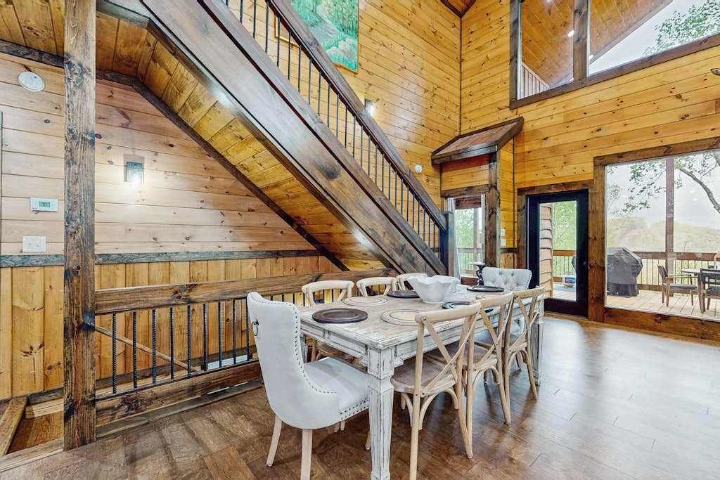 A wooden interior with a dining area, staircase, and large windows.