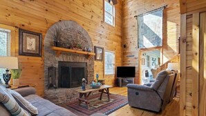 A log cabin interior with a stone fireplace, a sofa, a recliner, and a television. - Mountain Rivers Lodge (Mineral Bluff)