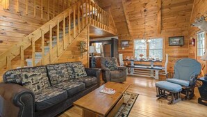 A log cabin interior with a wooden staircase, a sofa, a dining table, and a chair. - Mountain Rivers Lodge (Mineral Bluff)