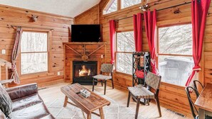 Ein rustikaler Blockhaus-Innenraum mit Kamin, Holzwänden, einem Fernseher und einer gemütlichen Sitzecke.