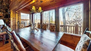 A wooden dining table with chairs, a chandelier, and large windows with a view of trees. - Lakeview Manor Cabin (Blue Ridge)
