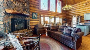 A log cabin interior with a stone fireplace, leather furniture, and large windows. - Lakeview Manor Cabin (Blue Ridge)
