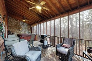 A covered outdoor deck with wicker furniture, a ceiling fan, and a stone wall. - Buckhorn Cabin Retreat (Sautee Nacoochee)