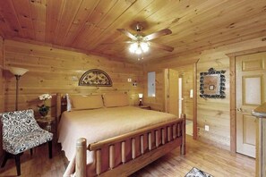 A wooden cabin bedroom with a bed, a chair, a ceiling fan, and a door. - Buckhorn Cabin Retreat (Sautee Nacoochee)