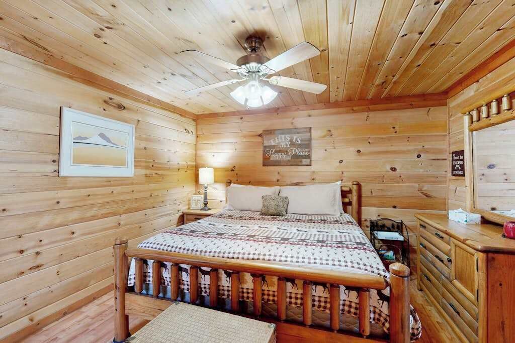 A wooden cabin bedroom with a bed, a ceiling fan, a nightstand, and a dresser.