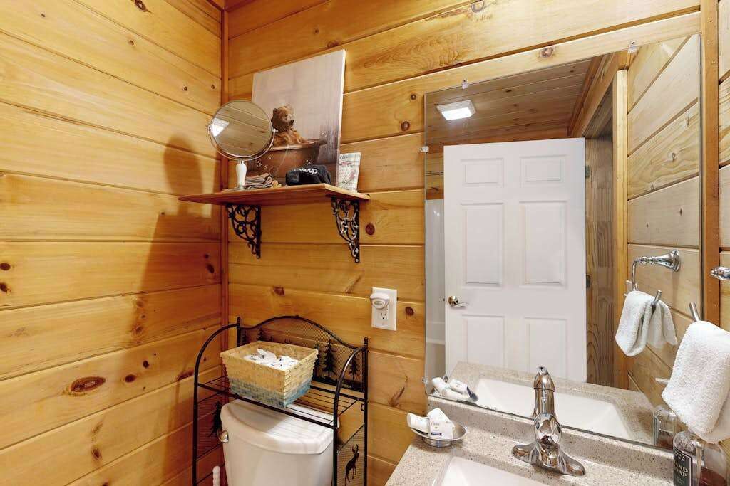 Un baño de cabaña de madera con lavabo, espejo y repisas con artículos de aseo.