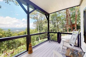 A covered porch with a view of a forest and distant landscape. - Ivy Mountain Top Stay (Hiawassee)