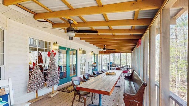 Eine überdachte Veranda mit einem langen Holztisch und Stühlen, einem Deckenventilator und Blick ins Freie.