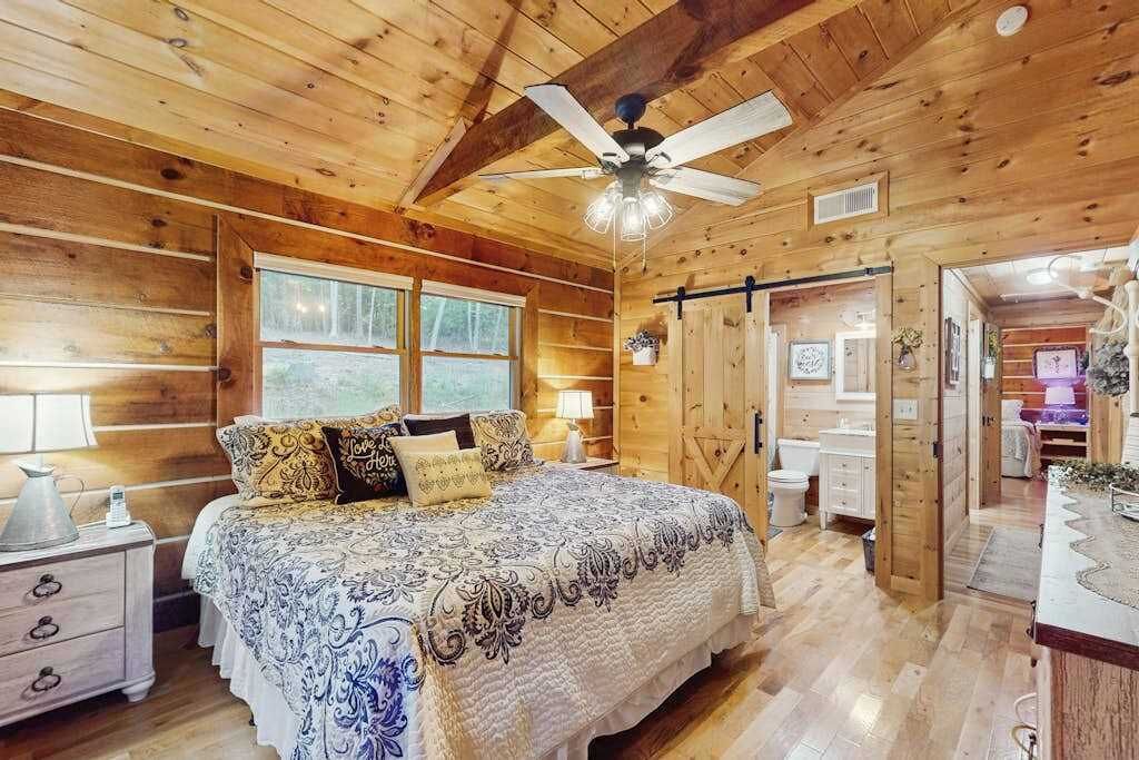 A wooden cabin bedroom with a bed, a nightstand, a ceiling fan, and a window.
