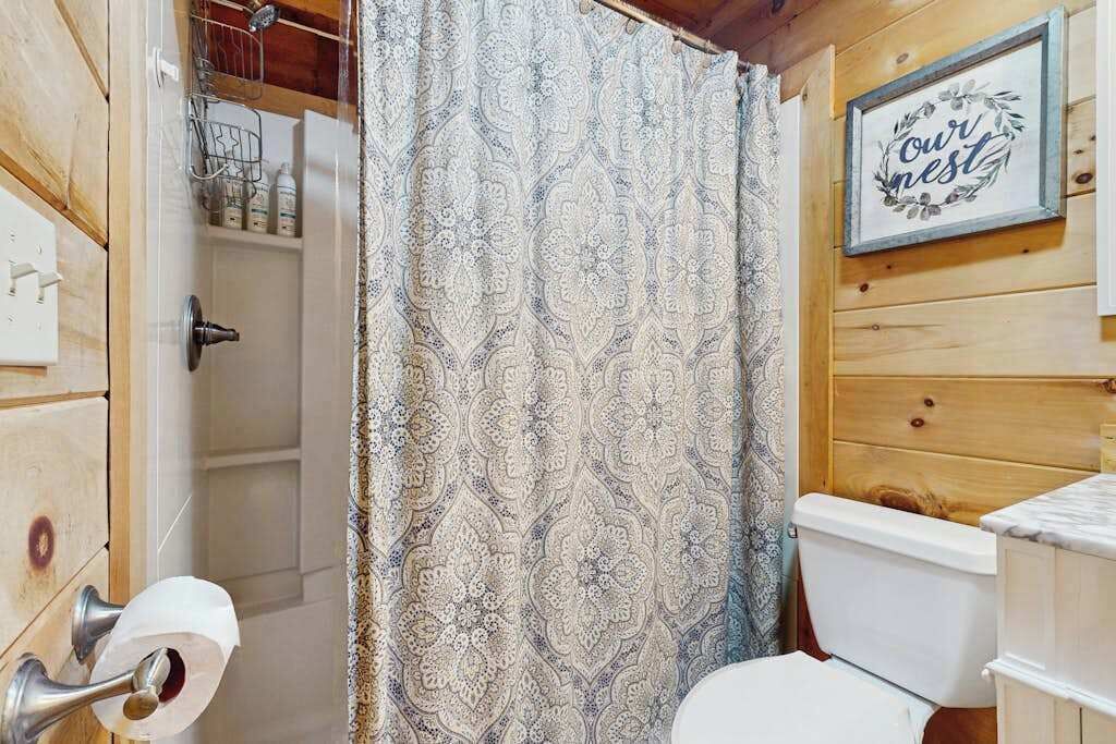 A bathroom with a patterned shower curtain, a toilet, a sink, and a framed sign on the wall.