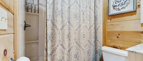 A bathroom with a patterned shower curtain, a toilet, a sink, and a framed sign on the wall.