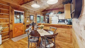 Interno di una baita in legno con zona pranzo, cucina e un'ampia finestra.