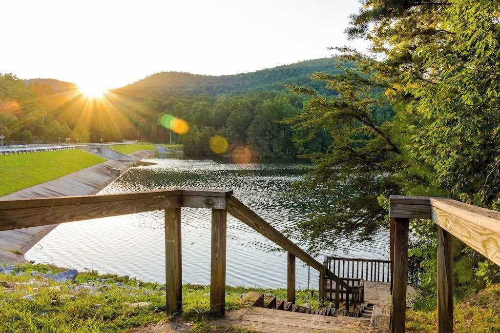 A wooden staircase leading down to a body of water, surrounded by greenery and hills.
