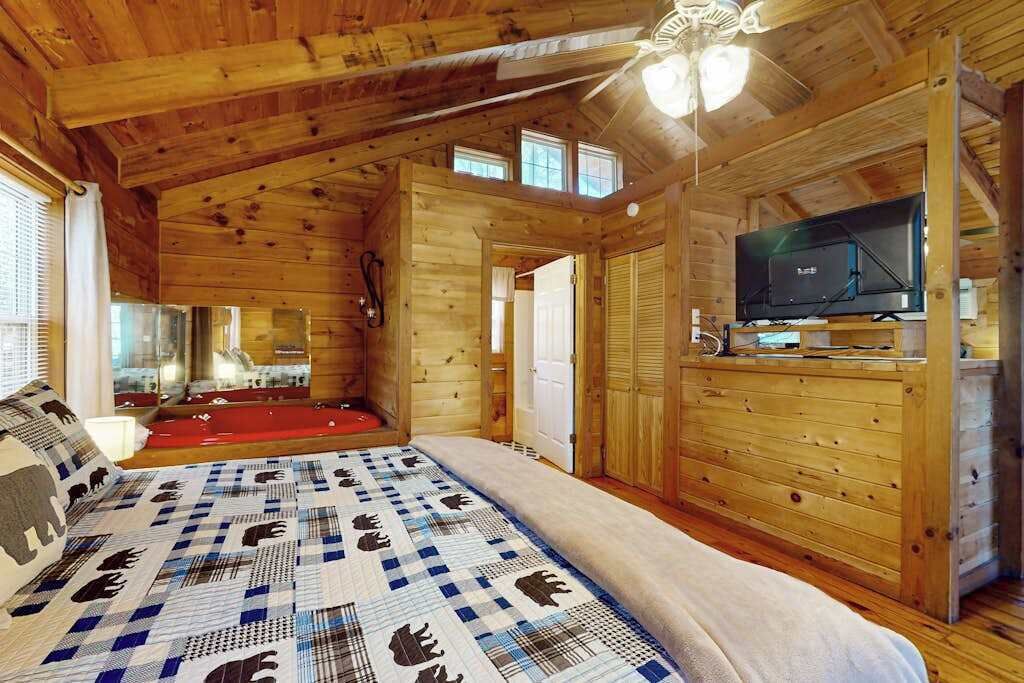A wooden cabin interior with a bed, a television, and a ceiling fan.