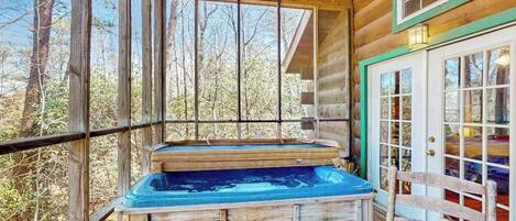 A wooden cabin with a hot tub, large windows, and a door with glass panels.