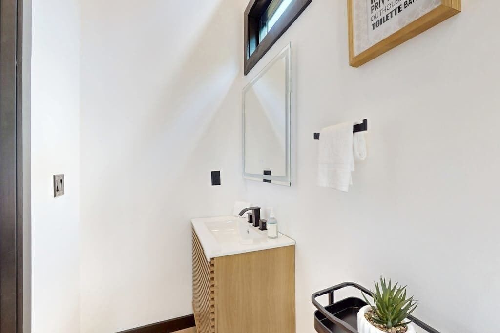Un baño moderno con tocador de madera, un espejo, un lavamanos, un perchero para toallas y una planta en maceta.