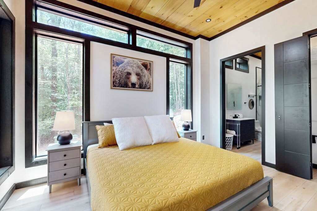 Een moderne slaapkamer met een groot bed, een nachtkastje, een spiegel en een deur naar een andere kamer.
