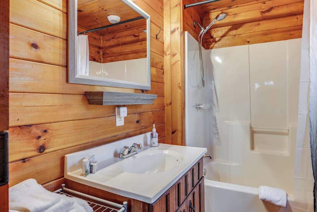 Een houten badkamer met een wastafel, spiegel en douche.