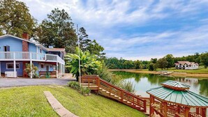 Une maison à deux étages avec un balcon, une terrasse en bois et un étang.