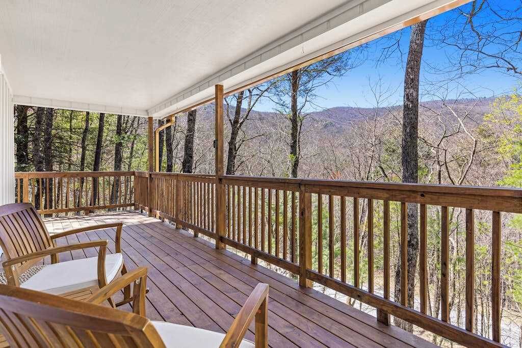 Une terrasse en bois, avec des chaises, d’où l’on peut admirer une chaîne de montagnes boisée.