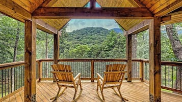 Eine Holzdar Terrasse mit zwei Schaukelstühlen, die auf einen bewaldeten Hang ausgerichtet sind.