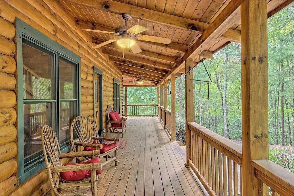 A log cabin with a porch, wooden chairs, and a ceiling fan.