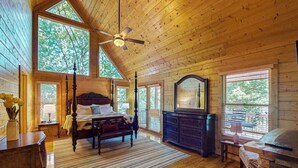 Interior de uma cabana de madeira com uma cama de dossel, um aparador e um ventilador de teto.